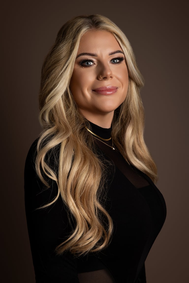 Professional headshot of a woman with long blonde wavy hair wearing a black top against a brown background