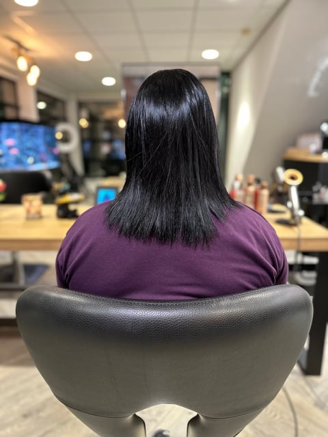 Vrouw met lang zwart haar in paars shirt aan bureau met monitoren