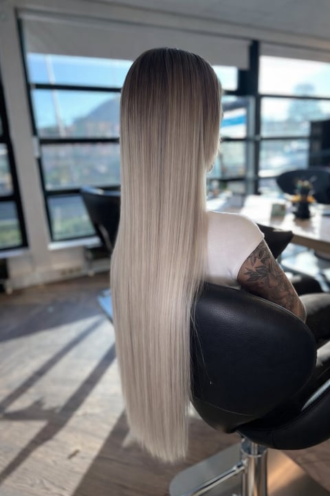 Vrouw met lang steil platinumblond haar in kantoorstoel met uitzicht op stad