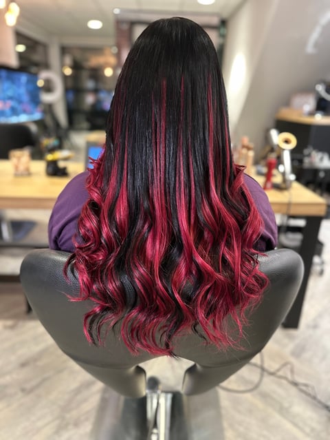 Vrouw met lang zwart en magenta ombre haar in salonstoel