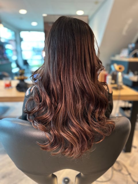 Vrouw met lang donkerbruin golvend haar in salonstoel