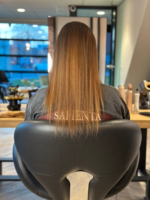 Vrouw met lang bruin haar in salonstoel, zijaanzicht