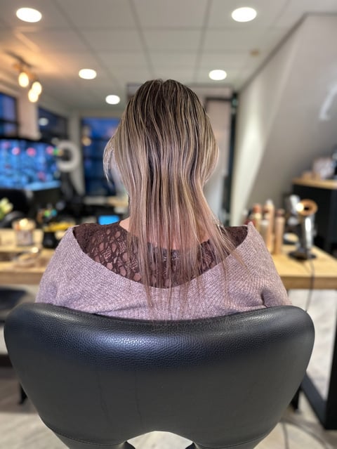 Vrouw met lang zilverblond haar in salonstoel, zijaanzicht