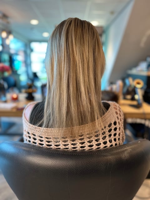 Achteraanzicht van vrouw met lang steil bruin haar met highlights in een beige gebreide trui in binnenruimte