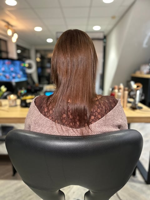 Vrouw met lang bruin haar in salonstoel, zijaanzicht