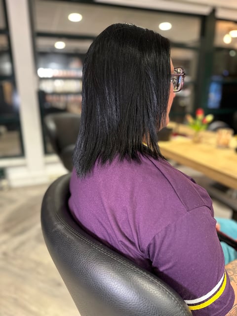 Vrouw met lang zwart haar in paars shirt in salon