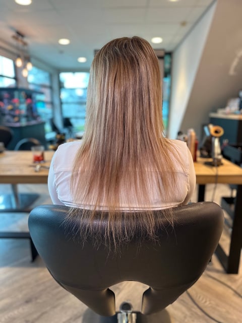 Vrouw met lang steil lichtbruin haar in salonstoel, zijaanzicht